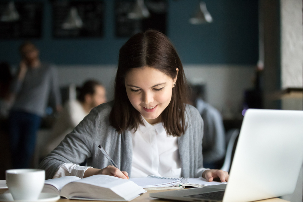 Image of a girl making notes in a book while sitting at a desk.